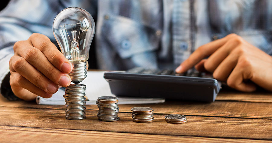 mão de um homem com moedas, calculadora e uma lampada em mãos demostrando que o consórcio é um bom investimento